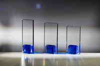 Thumbnail for Drei senkrechte Glasplaketten der „Glaspokal Dresden 3-er Serie 180x100 mm – 220x100 mm PK768130-28-3-E50“, jeweils mit blauer Grundfläche, sind in einer Reihe auf weißem Untergrund vor grauem Hintergrund angeordnet und erinnern an elegante Gravurschild-Embleme.